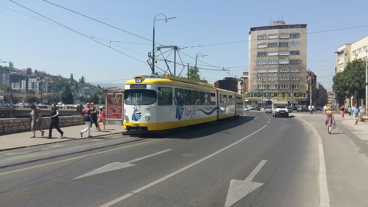 A yellow and white Sarajevo tram on the riverside road at Skenderija on a sunny day