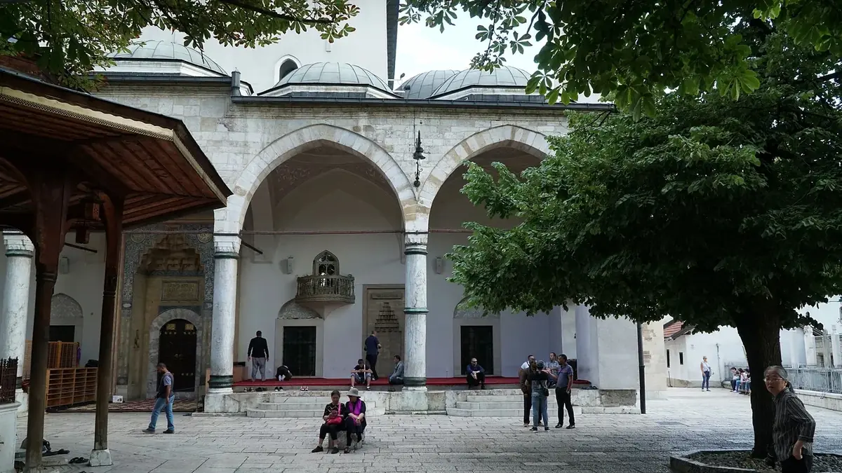 The stone porch and domes of the Gazi Husrev-beg Mosque in Baščaršija, Sarajevo, with visitors in the courtyard