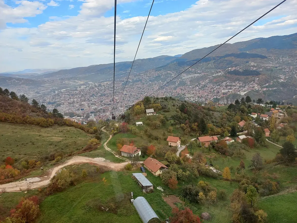 Sarajevo cable car view: looking down the cables over autumn trees and houses to the city in the valley