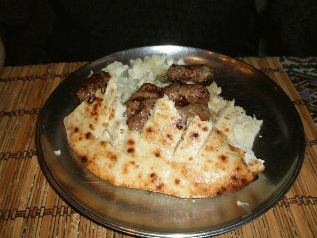 A portion of ćevapi in somun with chopped onion at Ćevabdžinica Petica in Sarajevo
