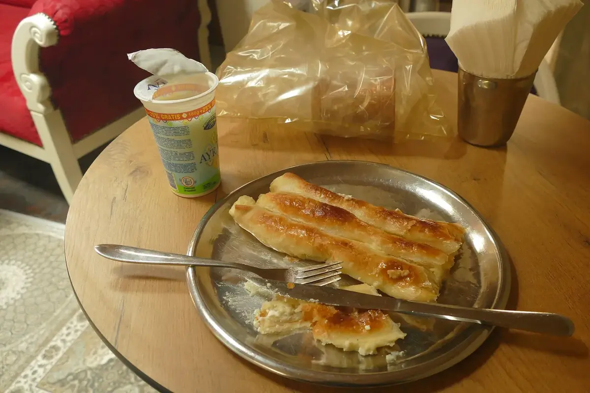 Rolled pita on a metal plate next to a cup of ayran at a café table in Sarajevo