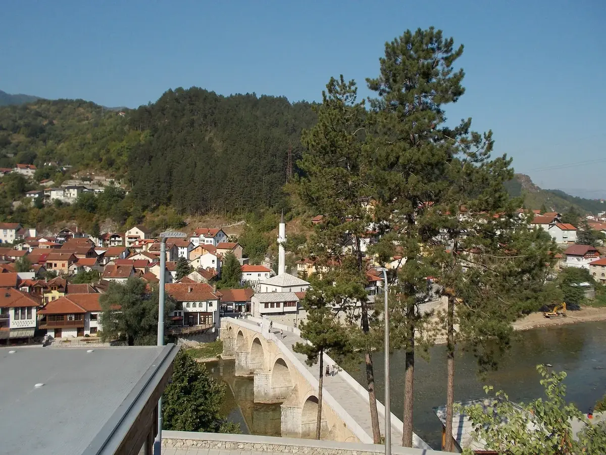 The old stone bridge over the river in Konjic, with red-roofed houses and wooded hills behind