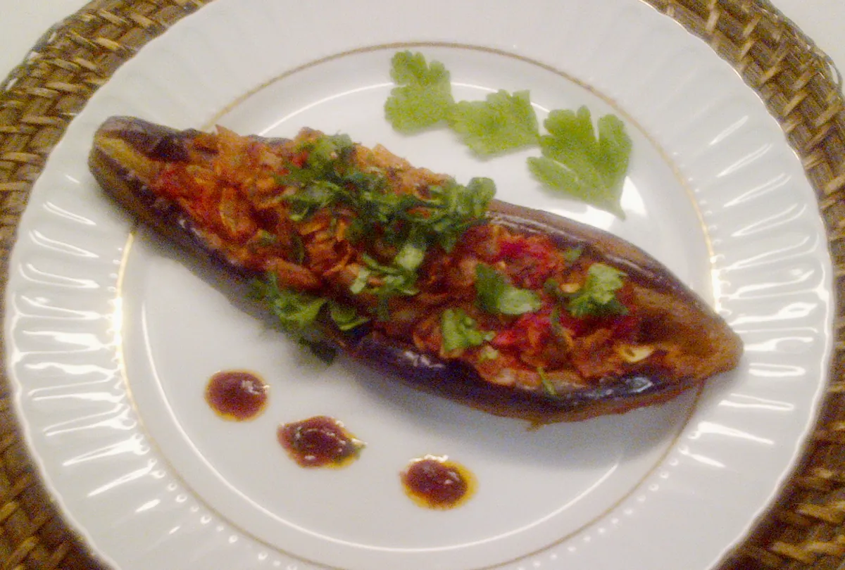 A baked aubergine stuffed with tomato and onion on a white plate