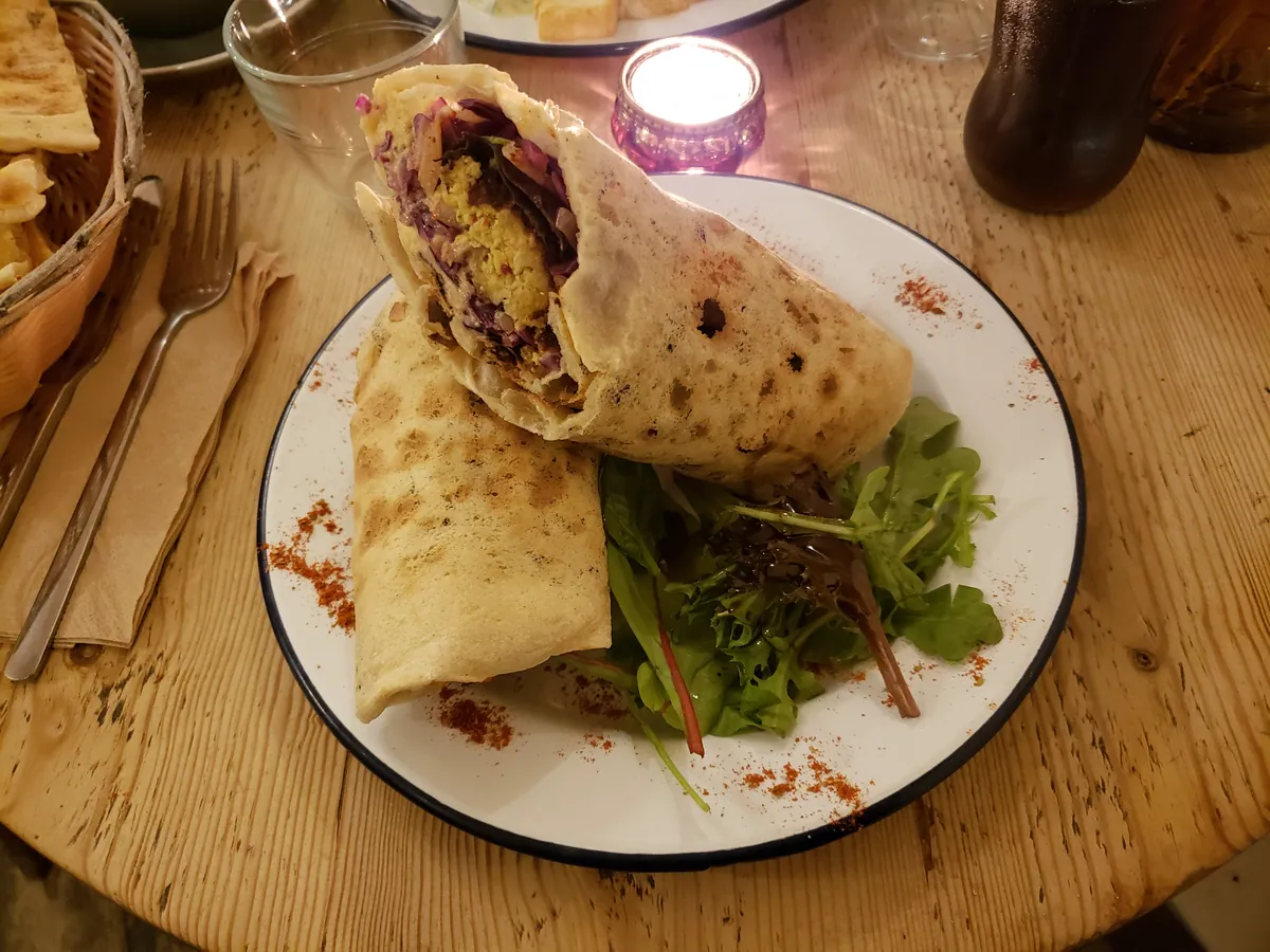 A falafel and hummus wrap cut in half, with salad leaves, on a plate