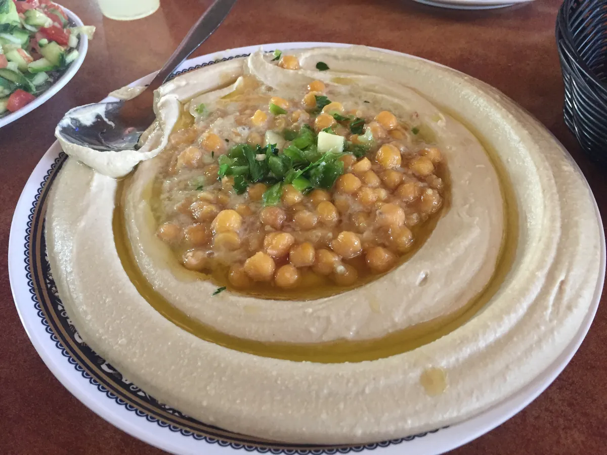 A plate of hummus topped with whole chickpeas, olive oil and parsley