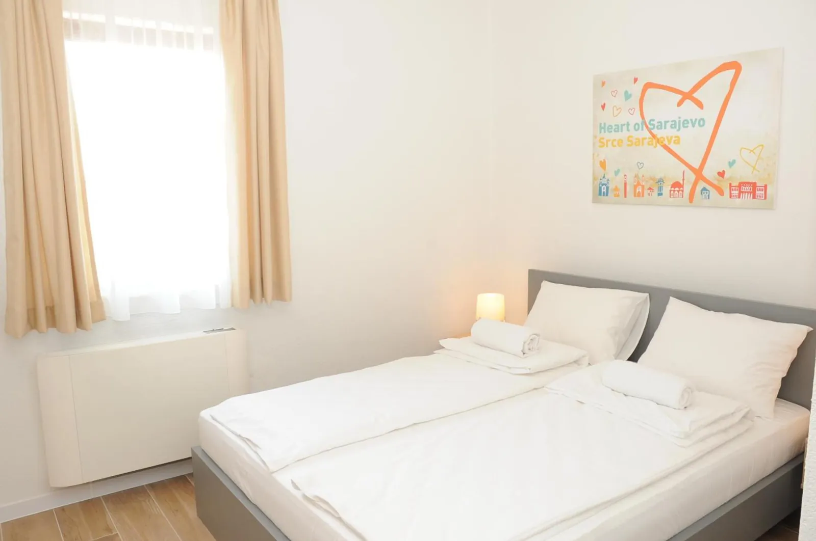 The queen bed by the window, under the Heart of Sarajevo print